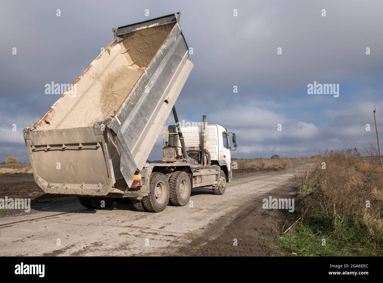dump-truck-with-a-raised-body-on-a-dirt-road-the-process-of-transportation-and-unloading-of-so...jpg